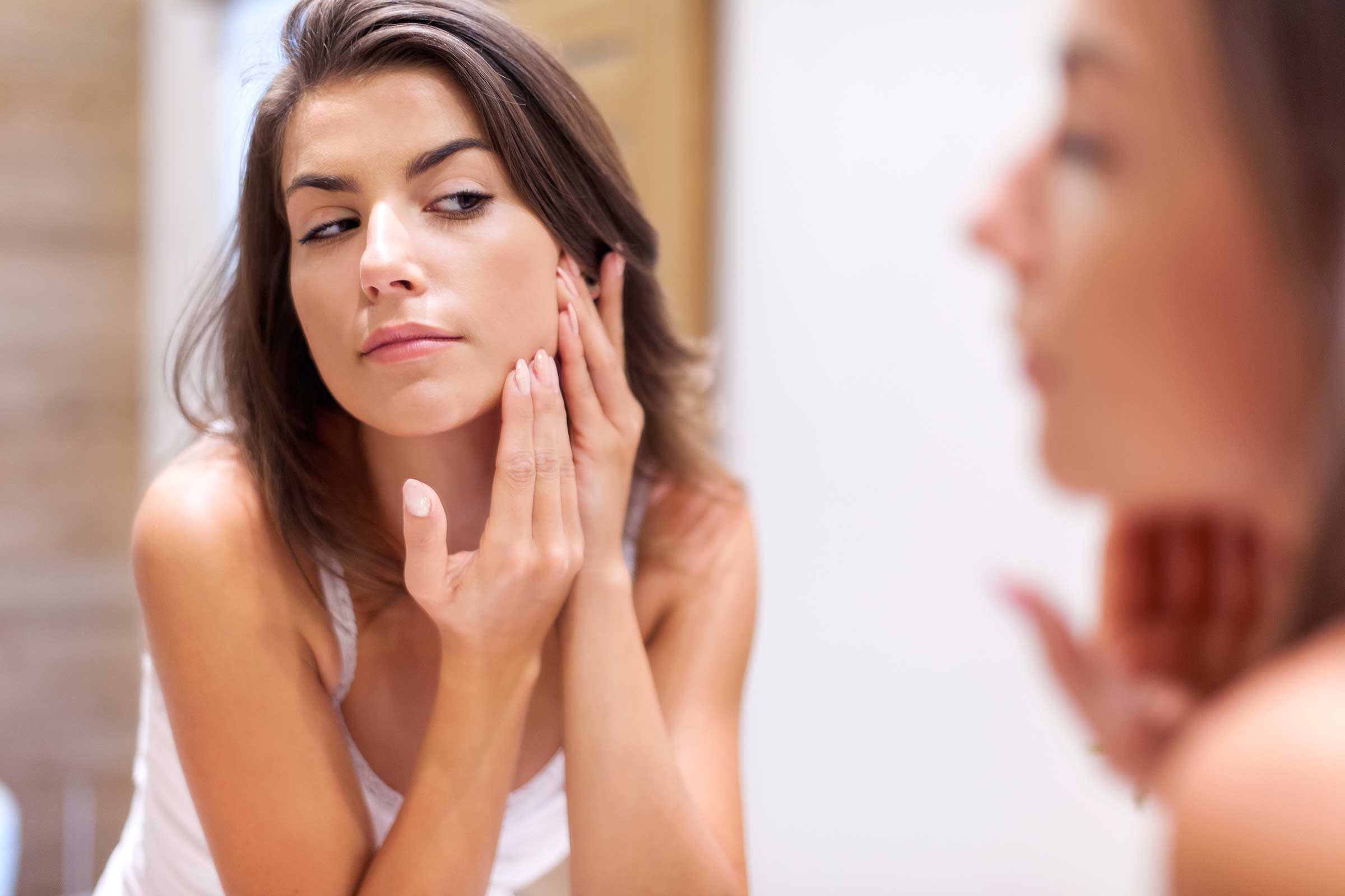 Young woman checking her skin in the mirror.