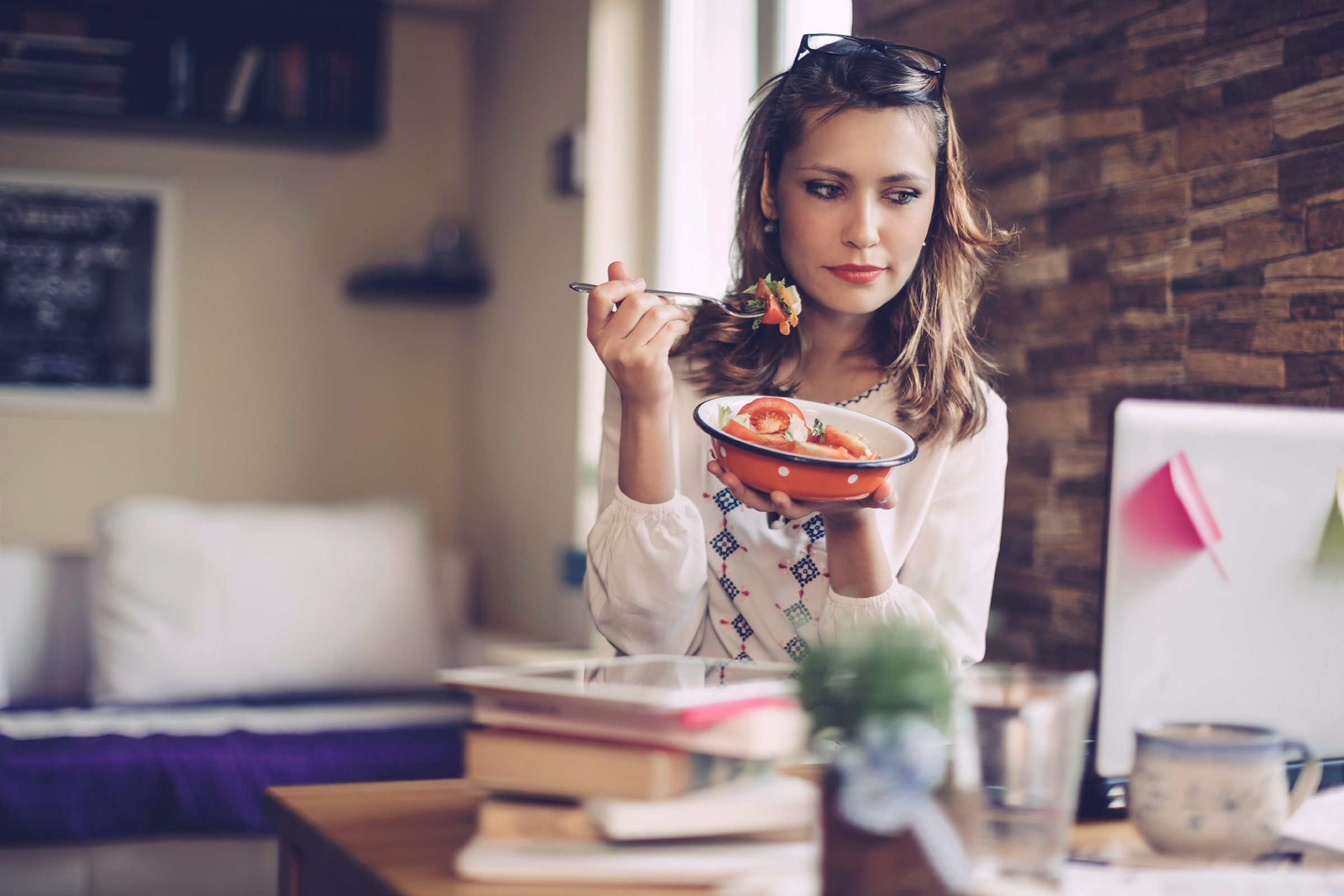 Woman eating from a bowl while looking at a computer