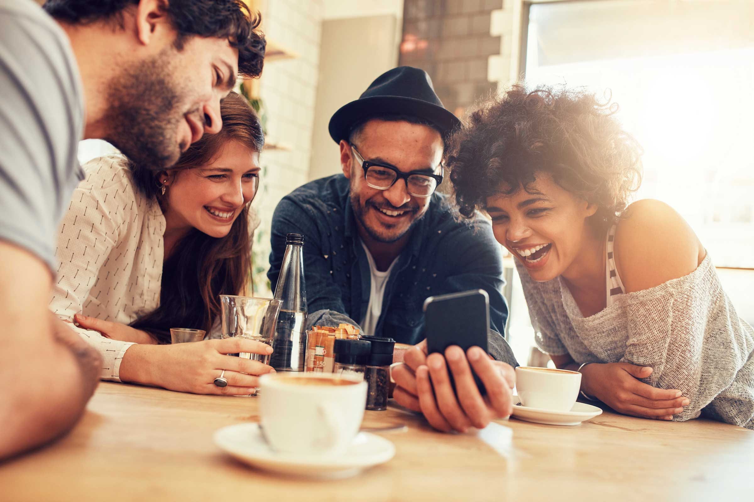 group of four people looking at smartphone and laughing