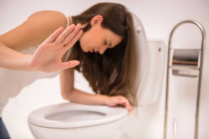 Ill woman leaning over the toilet bowl.