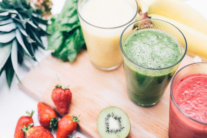 white, green, and red smoothies surrounded by fruit and veggies