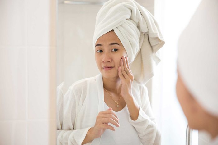 woman rubbing her face in mirror