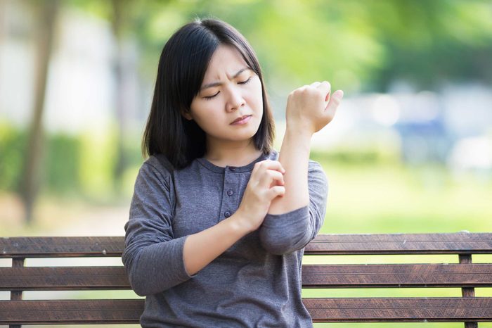 Woman sitting on a park bench scratching her arm.