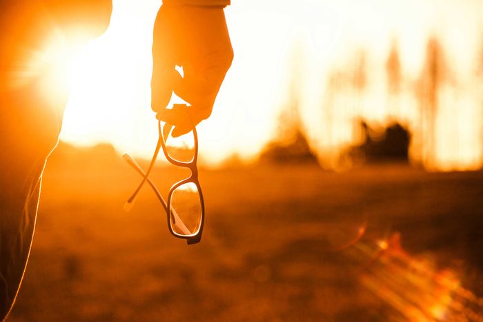 Person holding their glasses outside during a sunset.