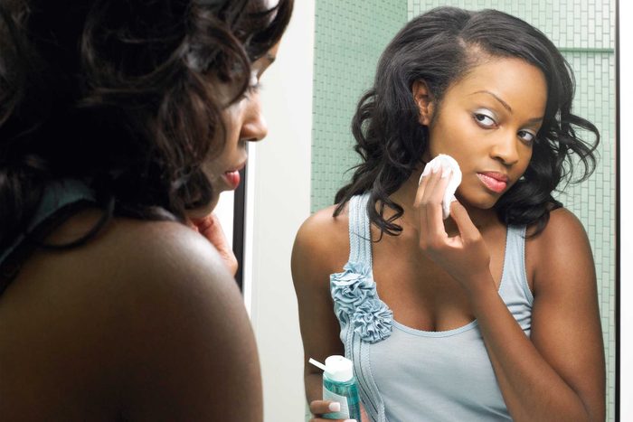 woman looking in a mirror applying beauty product with cotton pad