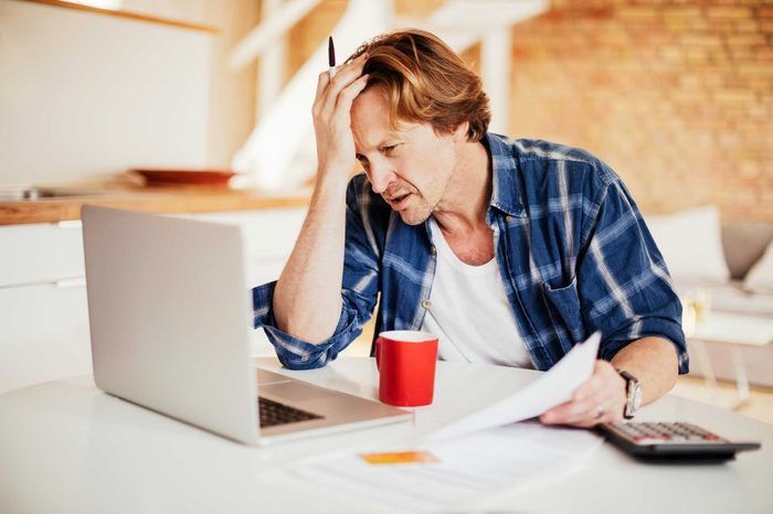 Man working at his laptop holding his forehead with one hand.