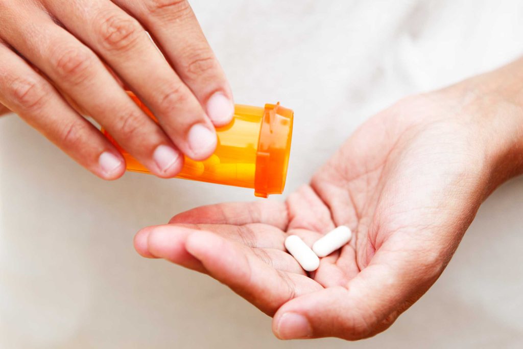 person shaking out tablets into their hand