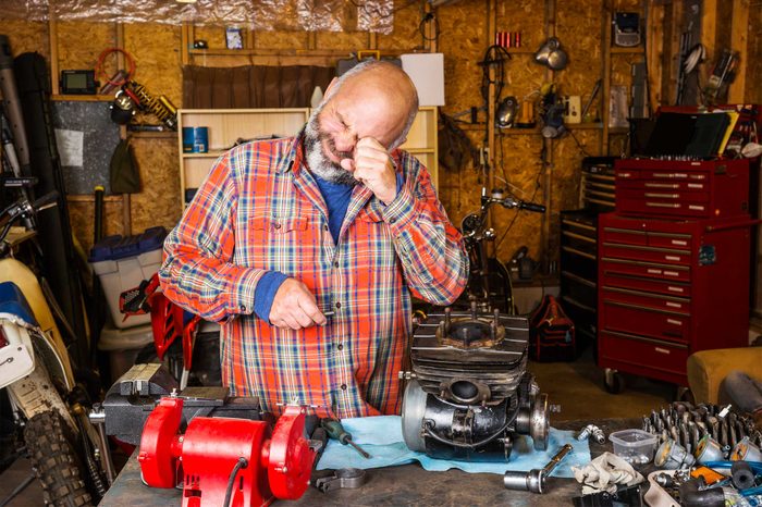 Man in his garage workshop rubbing his eye.