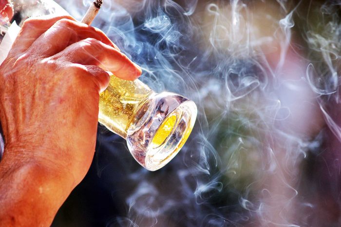 Man drinking a beer and holding a cigarette.
