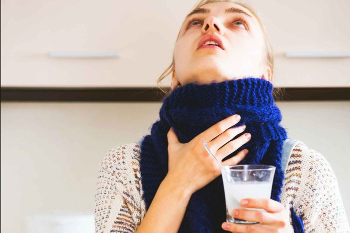 woman with scarf gargling with glass of salt water in hand