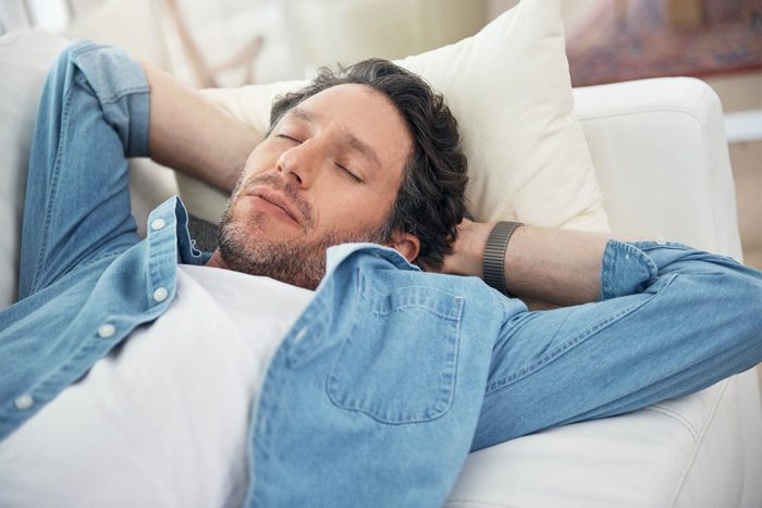 Man with hands behind his head asleep on a couch