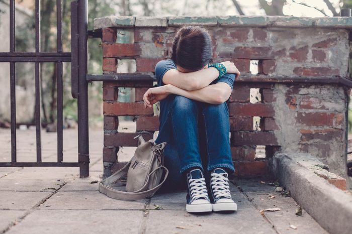 Woman on the ground, hugging knees, looking upset