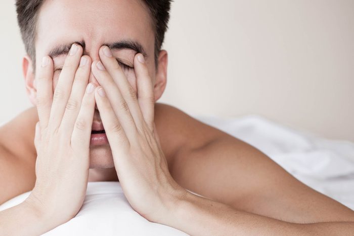 Sleepy man covering his face and lying on his bed.