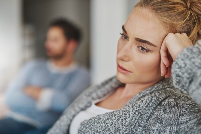 woman in focus resting her head on her hand; man out of focus in background