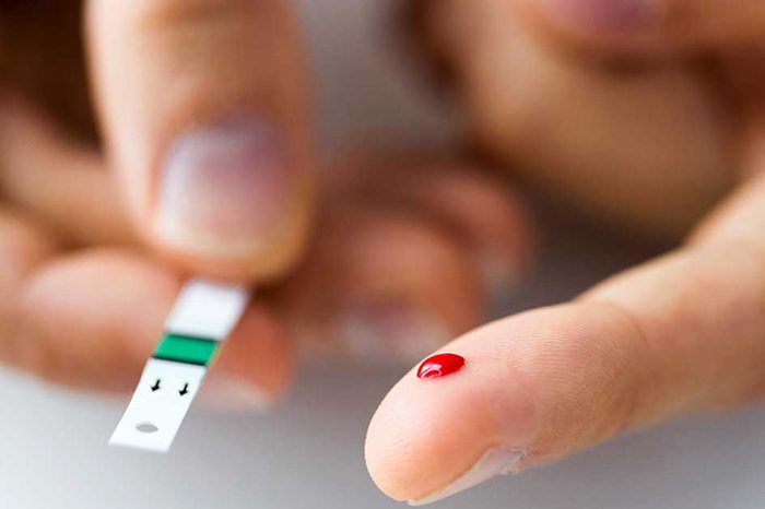 close-up of hands drawing blood from index finger for blood sugar test