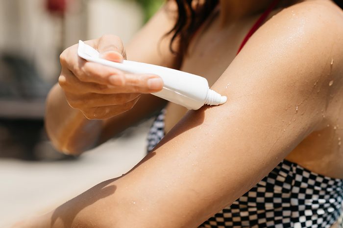 Woman applying sunscreen onto her skin from a tube.