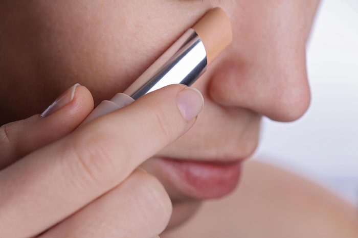 Woman applying a stick of concealer to her cheek.
