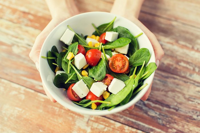 hands holding salad with tomatoes in white bowl