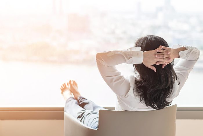 woman relaxing with hands behind head and looking out window
