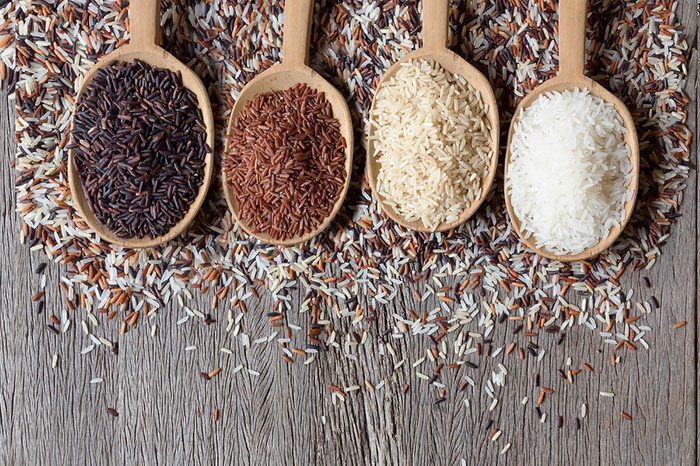 Wooden spoonfuls of black, white, brown, and red rice.
