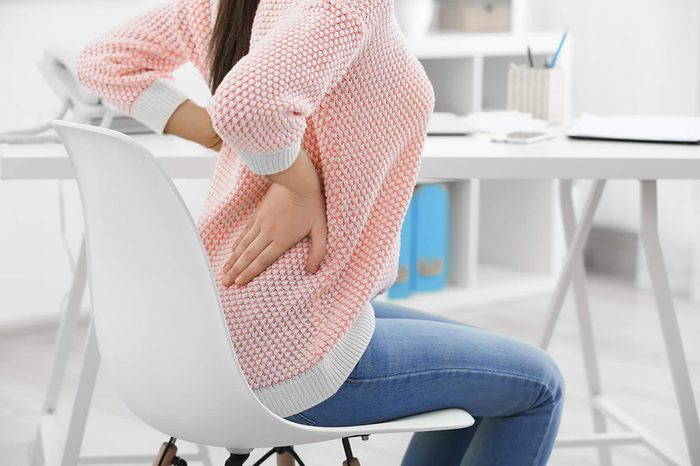 Woman in a chair holding her lower back because of kidney stone pain