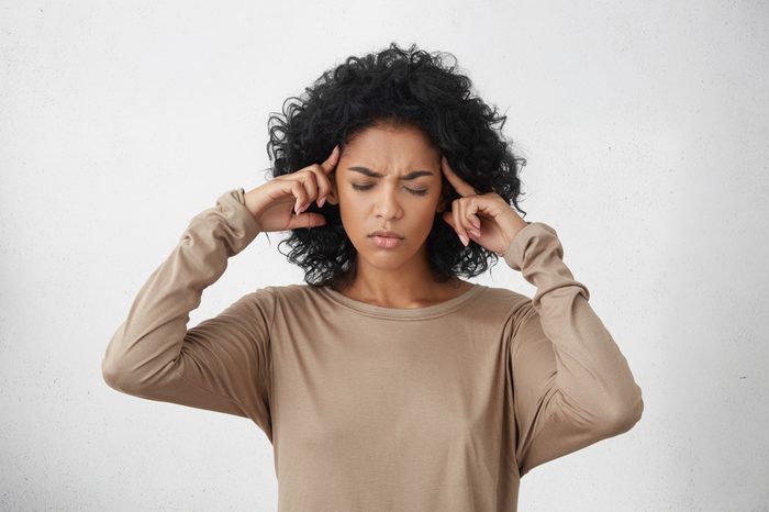 Constrained young mixed race female closing eyes tight and massaging temples with fingers to soothe unbearable migraine. Forgetful girl squeezing head with hands, trying hard to recollect something