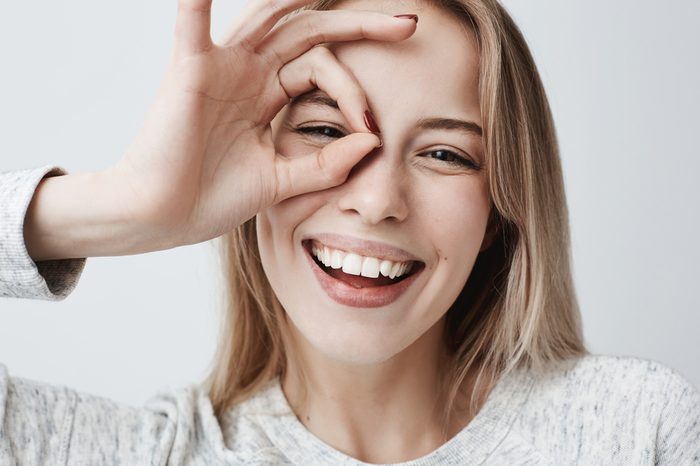 Woman smiling, looking at the camera through fingers in okay gesture