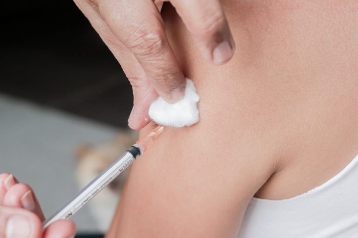 Asian woman is taking vaccine shot on her shoulder.