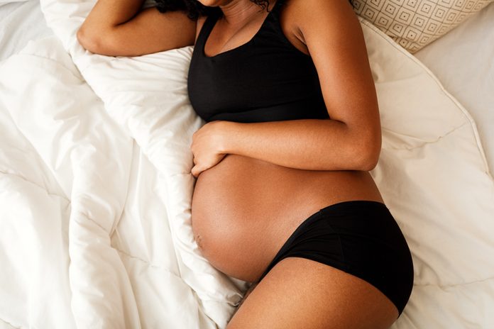 High Angle View Of Pregnant Woman Wearing Lingerie Lying On Bed At Home