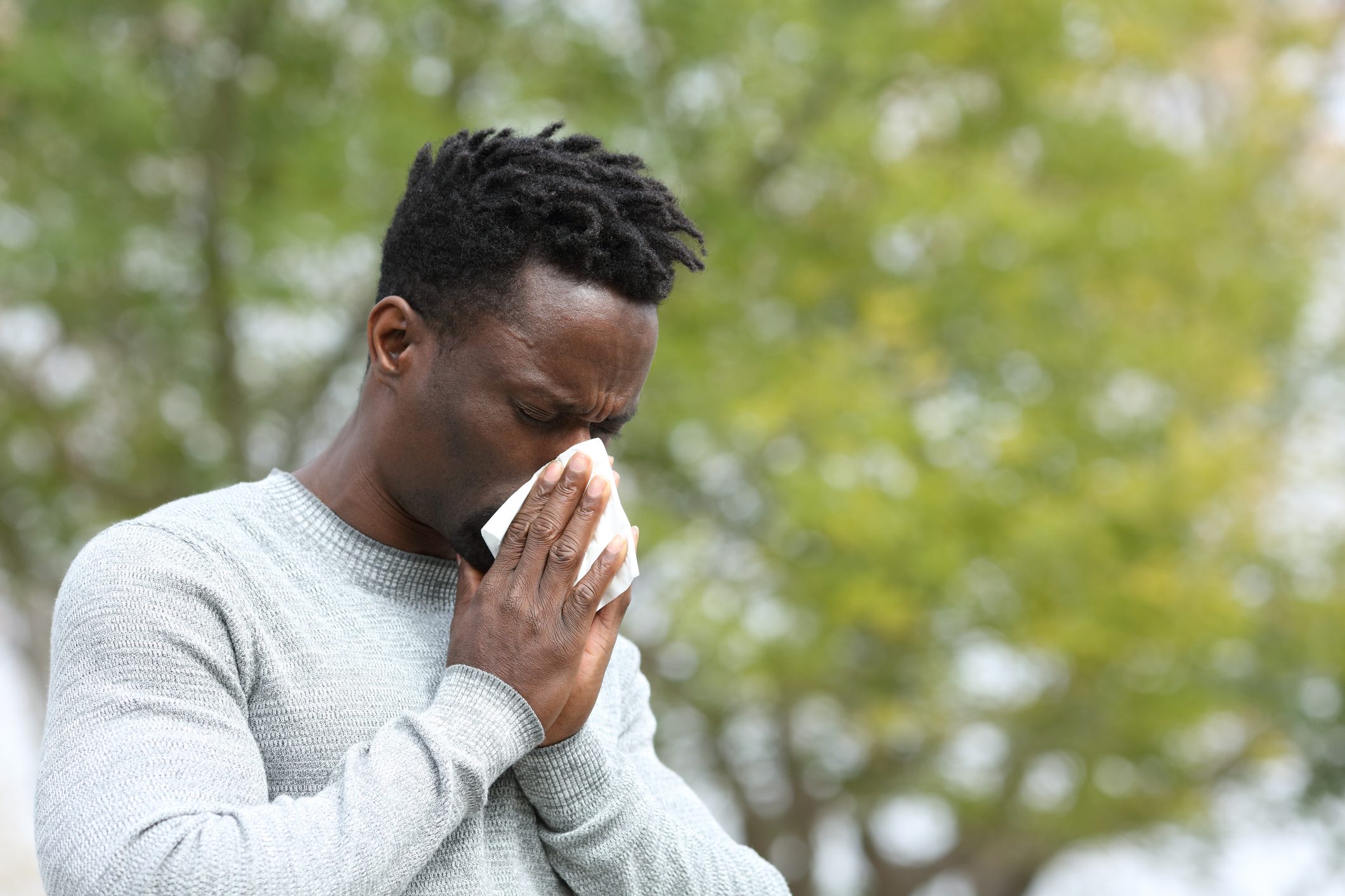Allergic man blowing on wipe in a park on spring season
