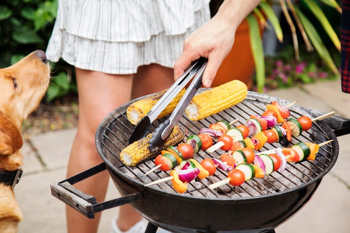 Close up of hand turning over food on barbecue, dog looks on.