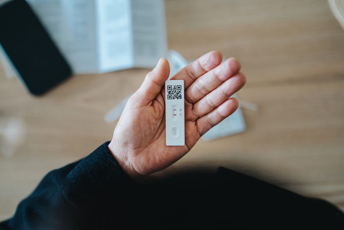 Overhead view of senior person carrying out a Covid-19 rapid lateral flow test at home. She is holding a positive Coronavirus rapid self test device, feeling worried