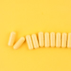 Many Yellow Pills Capsules On Yellow Color Background.