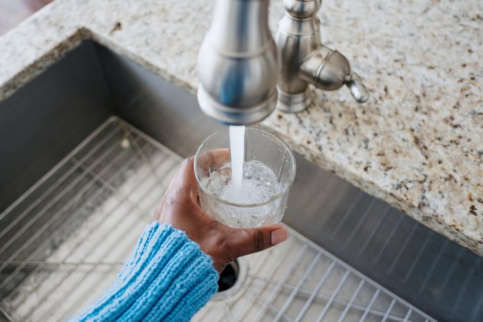 woman pouring water in glass from tap
