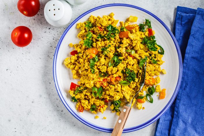 Tofu scramble with vegetables in a white plate, top view. Vegan Alternative fried eggs.