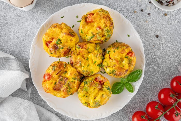 Egg muffins or egg bites with bacon, cheese, vegetables and herbs on a white plate on a concrete background. Healthy breakfast.
